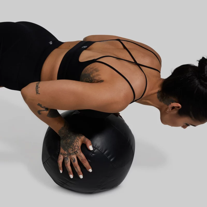 Kvinne i pushups-posisjon på medisinball. Hun har på seg en sort sports-bh og sorte shorts