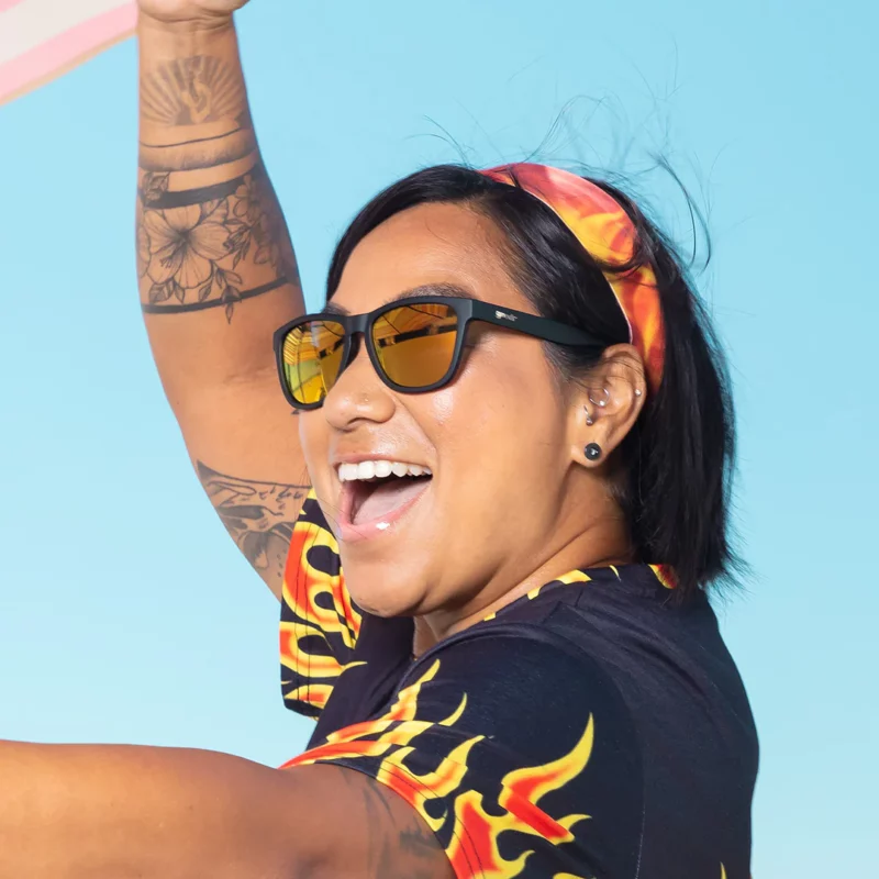 Kvinne som smiler, i flammeskjorte, med solbriller fra Goodr, Whiskey Shots