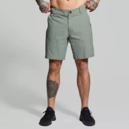 Beina til en mann i grønn shorts i teknisk stoff vendt med fronten mot kameraet. Shortsen har en lomme på hver side. Den har glidelås og knapp, samt hemper til belte.