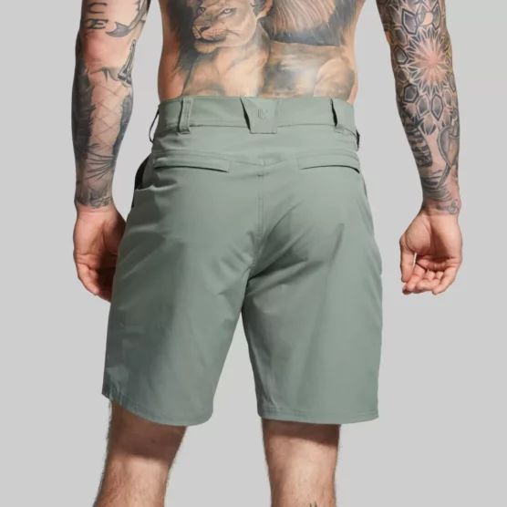 Beina til en mann i grønn shorts i teknisk stoff med ryggen mot kameraet. Shortsen har en lomme på hver side. Den har hemper til belte.
