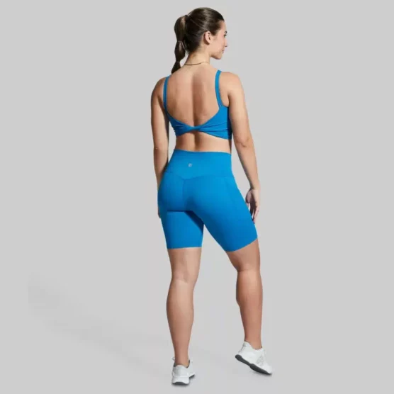 Dame i blå shorts og sports-bh i teknisk stoff med twisted rygg.