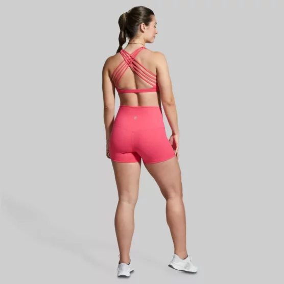 Dame i rosa sports-bh og shorts i teknisk stoff med ryggen mot kameraet. Sports-bhen har 4 stropper på hver side som krysser hverandre litt over skulderbladene.