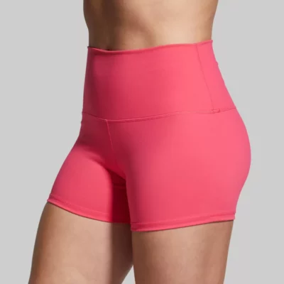 Booty short Beina til en dame i rosa shorts i teknisk stoff som står skrått vendt mot kameraet. Shortsen er høy i livet.