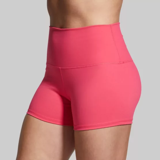 Beina til en dame i rosa shorts i teknisk stoff som står skrått vendt mot kameraet. Shortsen er høy i livet. Booty short