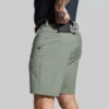 Beina til en mann i grønn shorts i teknisk stoff vendt med den venstre siden mot kameraet. Shortsen har en lomme på foran og en bak. Lommen bak har glidelås. Den har hemper til belte.