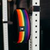 Løftebelte fra merket 2Pood Performance som henger på en rigg. Beltet har striper i Pride-fargene.