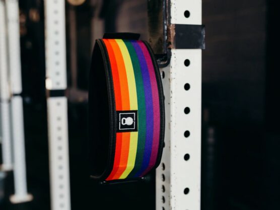 Løftebelte fra merket 2Pood Performance som henger på en rigg. Beltet har striper i Pride-fargene.