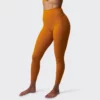 treningstights, Beina til en dame i oransje tights i teknisk stoff som står skrått vendt mot kameraet. Tightsen er høy i livet.