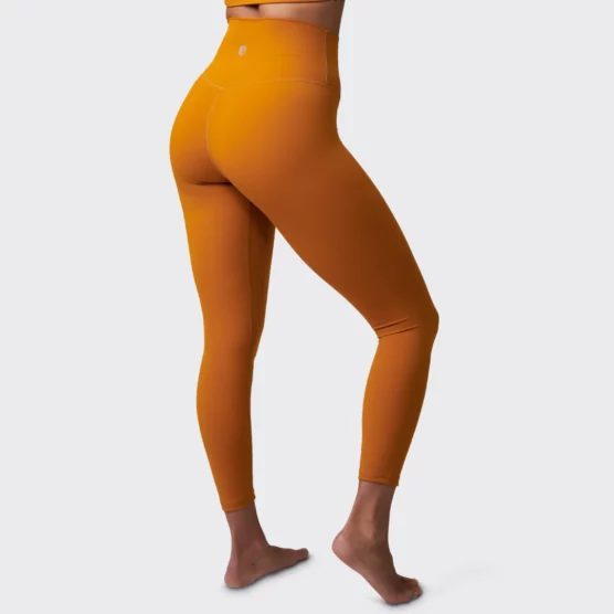 Beina til en dame i oransje tights i teknisk stoff som står med ryggen skrått mot kameraet. Tightsen er høy i livet.