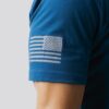 Armen til en mann i blå t-skjorte som står med siden mot kameraet. På ermet er det bilde av det amerikanske flagget i hvitt.