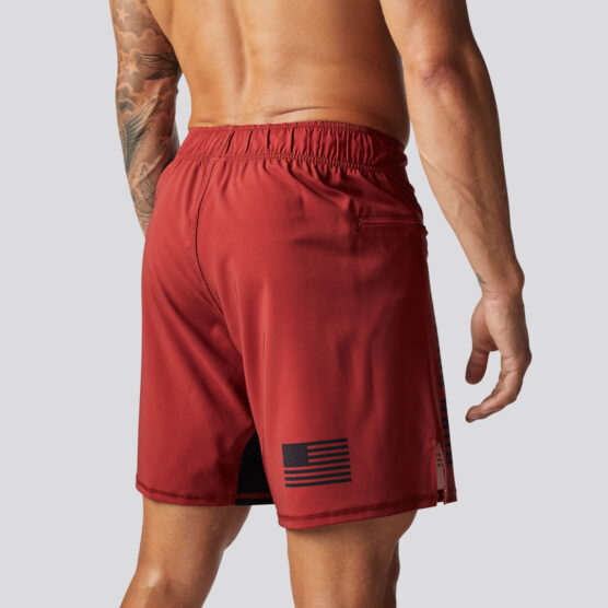 Beina til en mann i rød shorts står med ryggen skrått mot kameraet. Det er bilde av det amerikanske flagget i sort nede på det høyre låret. På innsiden av det venstre låret er det en sort stripe.