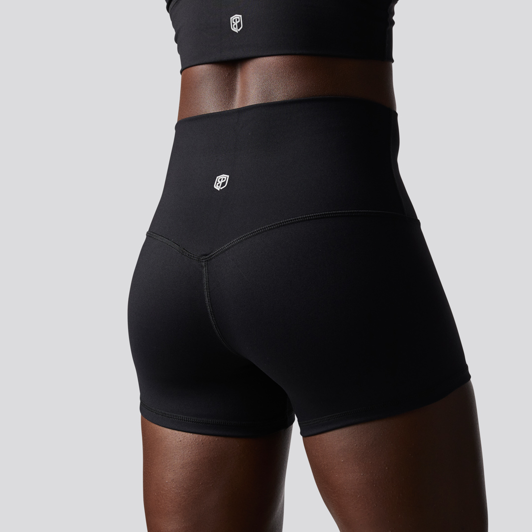 Beina til en dame i sort shorts i teknisk stoff som står med ryggen mot kameraet. Shortsen er høy i livet.