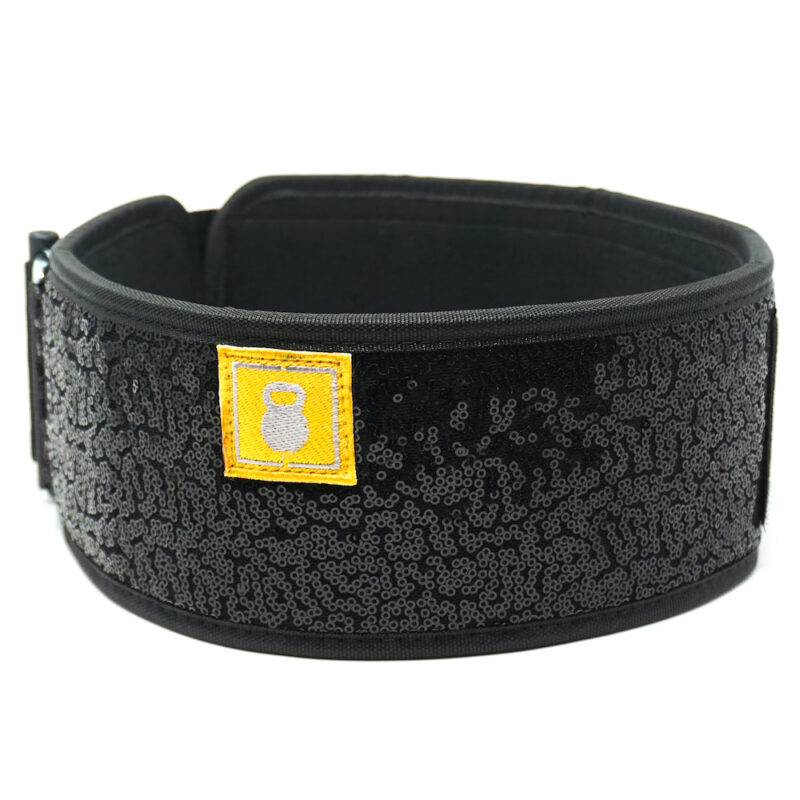 Løftebelte fra merket 2Pood Performance. Beltet har en sort kant og er dekket med sorte paljetter. Det har et lite gult merke med en hvit kettlebell.