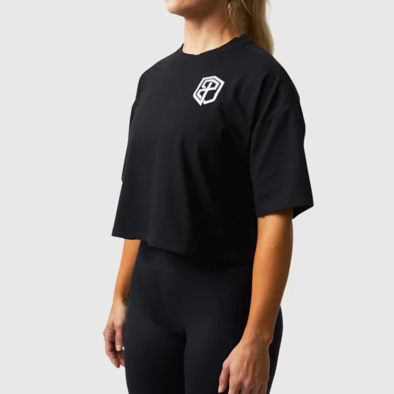 Kvinne avbildet skrått forfra med sort t-skjorte som rekker til midjen, med en grå logo på venstre bryst.