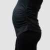Gravid dame i sort treningssinglet i teknisk stoff med siden mot kameraet. Singleten er rysjet på siden.
