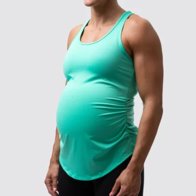 gravidetopp, Gravid dame i mintgrønn treningssinglet i teknisk stoff som står skrått vendt mot kameraet. Singleten er rysjet på siden og den har brede stropper over skuldrene.