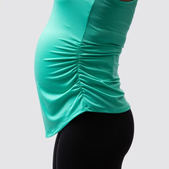Gravid dame i mintgrønn treningssinglet i teknisk stoff med siden mot kameraet. Singleten er rysjet på siden.