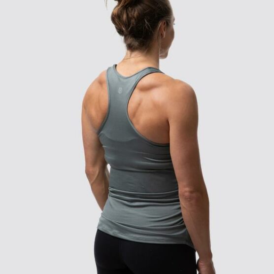 Gravid dame i grå treningssinglet i teknisk stoff med ryggen skrått mot. Det er racerback rygg og brede stropper over skuldrene.