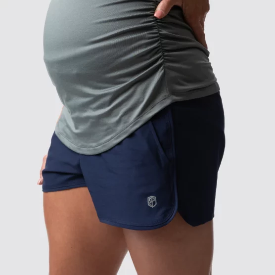 mammashorts, Beina til en gravid dame i blå shorts i teknisk stoff som står med siden vendt mot kameraet. Shortsen har lomme på sidene. Aktive mødre