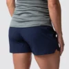 Beina til en gravid dame i blå shorts i teknisk stoff som står med ryggen mot kameraet.