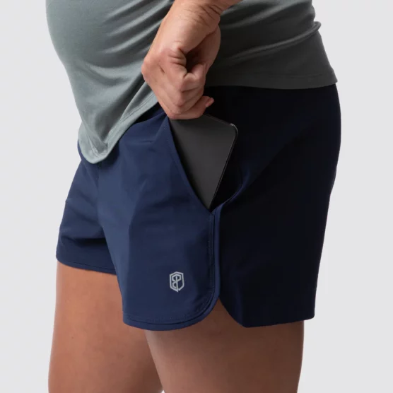 Beina til en gravid dame i blå shorts i teknisk stoff som står med siden vendt mot kameraet. Shortsen har lomme på sidene.