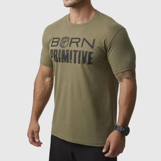 Mann i grønn t-skjorte som står skrått vendt mot kameraet. Det står "Born Primitive" med sort tekst på brystet.