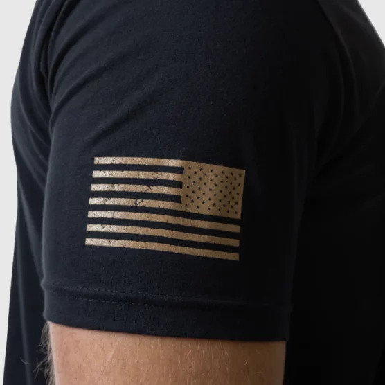 Mann i sort t-skjorte med den høyre siden vendt mot kameraet. På ermet er det bilde av det amerikanske flagget i gull.
