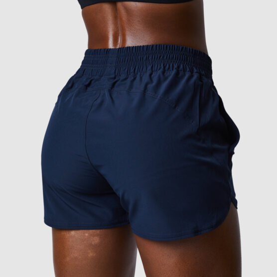 Beina til en dame i blå shorts i teknisk stoff som står med ryggen mot kameraet. Shortsen har bred strikk øverst i livet.