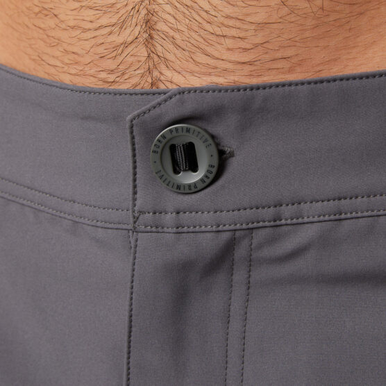 Mann i mørkegrå shorts i polyester vendt med fronten mot kameraet. Den har glidelås og knapp.