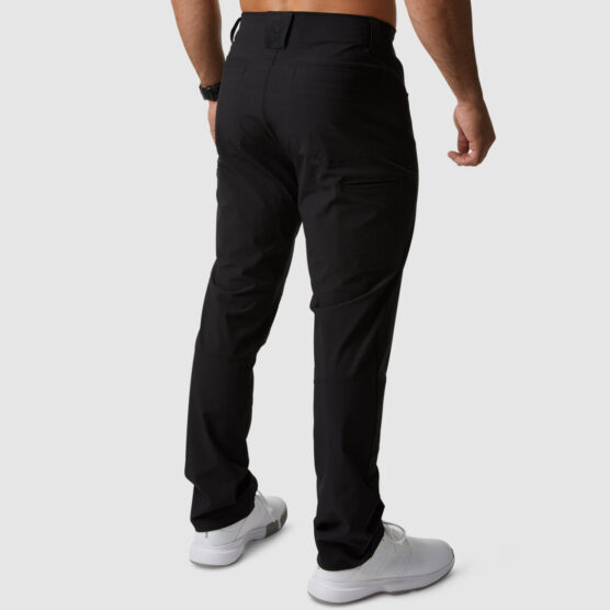 Beina til en mann i sort bukse i teknisk stoff som stor med ryggen mot kameraet. Den har hemper til belte og en lomme på hver side av rumpa.