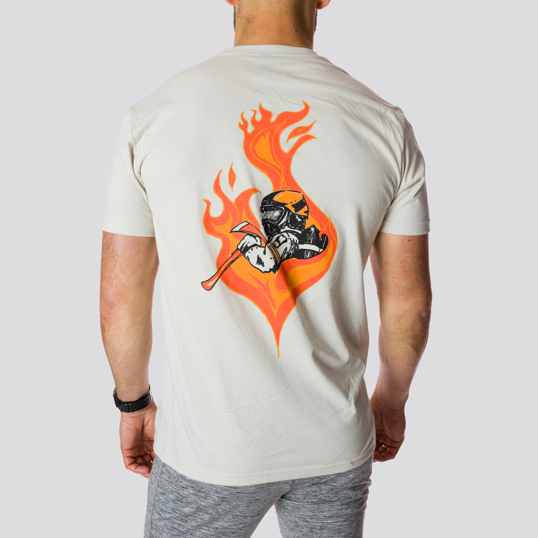 En mann med sandfarget t-skjorte som står med ryggen mot kameraet. På ryggen er det bilde av en brannkonstabels overkropp inne i en flamme.