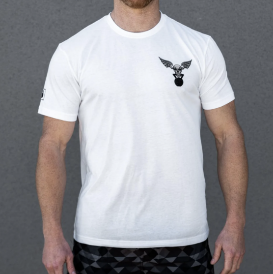 Mann i hvit t-skjorte fra 2Pood Performance som står vendt mot kameraet. Det er bilde av en hodeskalle med vinger og som holder en kettlebell i munnen på den venstre siden av brystet.