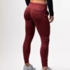 Beina til en dame i en burgunder joggebukse i teknisk stoff som står med ryggen mot kameraet. Buksa har lomme på hver side bak.