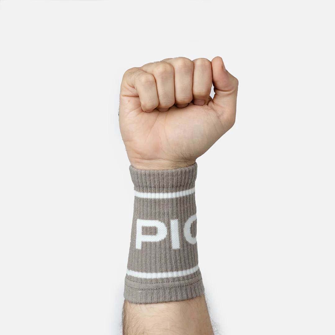 Wristbands fra Picsil på en arm. De er brune med hvite striper og teksten "Picsil" i hvit farge.