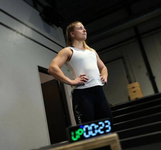 Dame som står med en mini gym timer på en boks foran seg. Displayet viser "Up" og "0:23" sekunder igjen. Up står i grønt og tallene i blått.