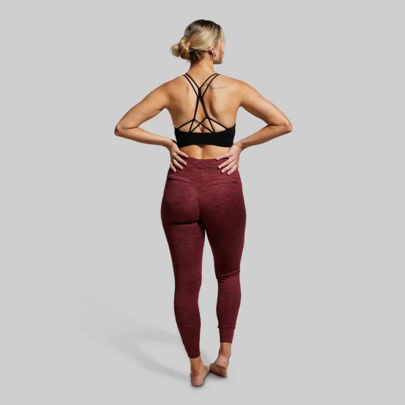 Kvinne med ryggen vendt mot kamera, iført en burgunderrød treningsbukse/joggebukse og sort sportsbh