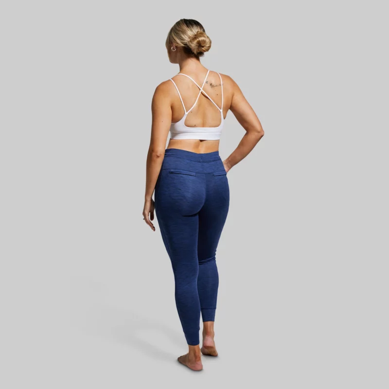 Kvinne med ryggen vendt mot kamera, iført en marineblå treningsbukse/joggebukse og hvit sportsbh.