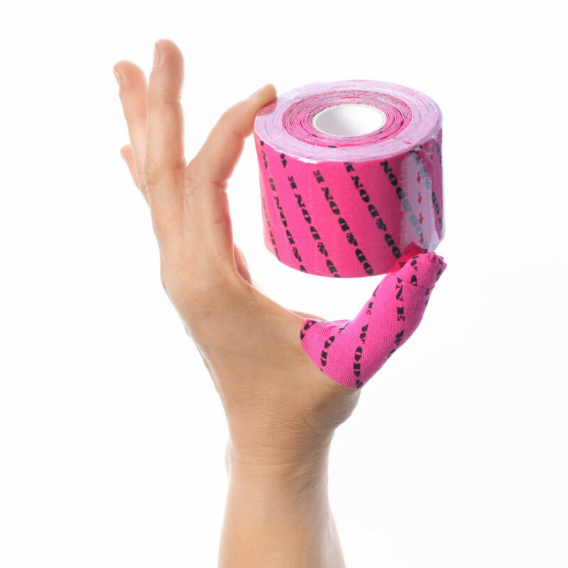 En hånd som holder en rull med rosa tommeltape fra merket Wod & Done. På tapen står det "Wod & done" med sort tekst. Tommelen er tapet.