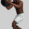 Mann i hvit shorts med gråspraglete mønster som kaster en treningsball.
