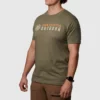 Mann i ført militærgrønn T-skjorte avbildet skrått forfra, med skriften Born Primitive i orange, og Outdoor i hvitt. På brystet. Det også en loge ved siden av.