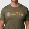 Mann i ført militærgrønn T-skjorte med skriften Born Primitive i orange, og Outdoor i hvitt. På brystet. Det også en loge ved siden av.