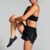 Kvinne avbildet i en sort shorts med 5 små kvadrater på siden av hoften og strikk i livet