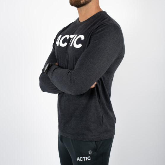 Mann avbildet skrått forfra med armene i kryss iført mørk grå langermet genser med ACITC skrevet i hvit over brystet