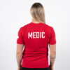 Kvinne avbildet bakfra iført en rød t-skjorte med skriften MEDIC skrevet mindt på, øverst på ryggen i hvit.