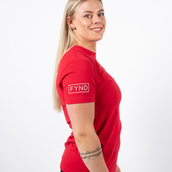 Kvinne avbildet fra siden iført en rød t-skjorte med skriften FYND skrevet i et rektangel i hvit på overarmen.