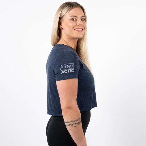 Kvinne avbildet fra siden iført en mørk blå t-skjorte som rekker til hoftekammen med FYND og ACITC skrevet i lys grå på overarmen