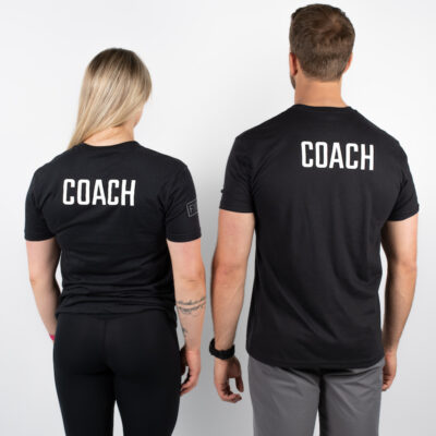 En mann og en kvinne avbildet bakfra iført sorte t-skjorter med skriften COACH i hvit skrift på øvre dele av ryggen.