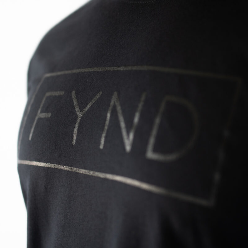 Detaljbilde av brystet på en langermet sort genser med teksten FYND skrevet i et rektangel i sort.