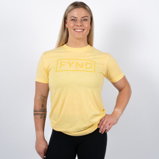 Kvinne avbildet forfra, iført en lys gul t-skjorte med skriften FYND skrevet i et rektangel med gul skrift midt på brystet.