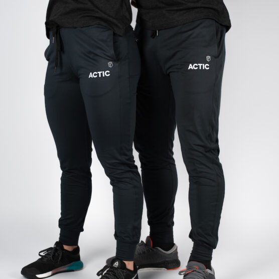 Beina til mann og kvinne avbildet skrått forfra iført sorte lange bukser med ACTIC skrevet i hvit øverst på høyre lår